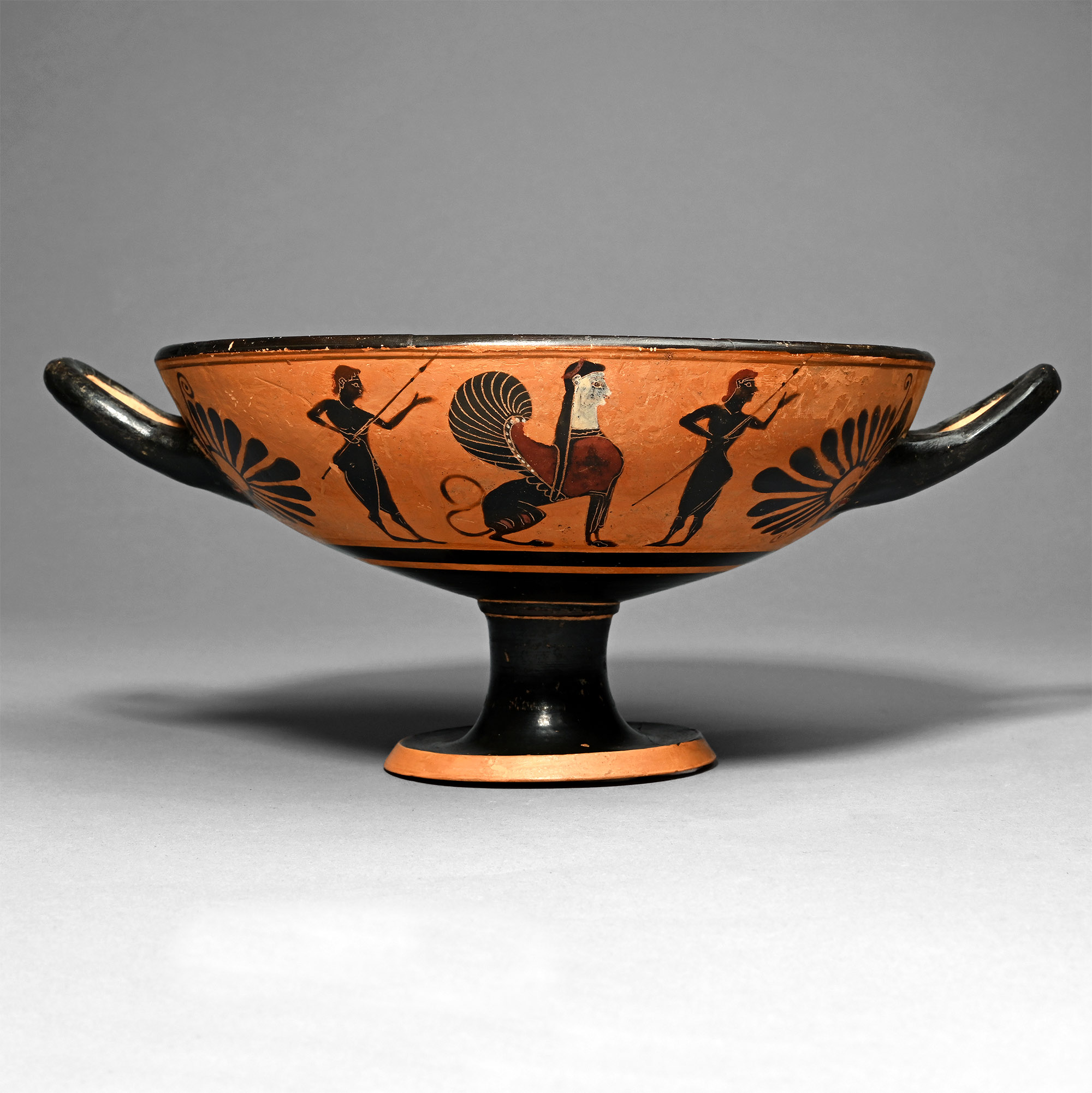 An Attic black-figure kylix, nude youths flanking a sphinx