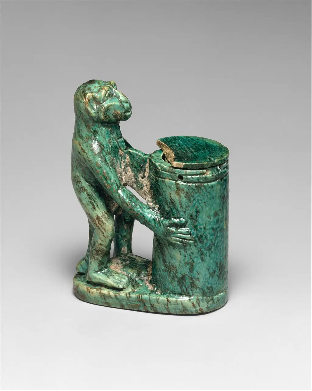 An Egyptian kohl tube modelled as a monkey clutching a vessel