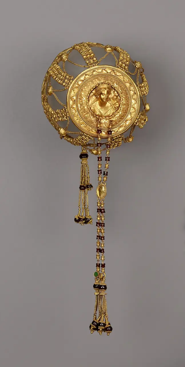 A Hellenistic gold hairnet, its domed net of spool-bead chains rising to a medallion of Aphrodite with a small Eros