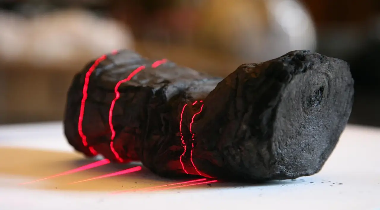 A carbonized Herculaneum scroll under red laser scanning lines in the laboratory