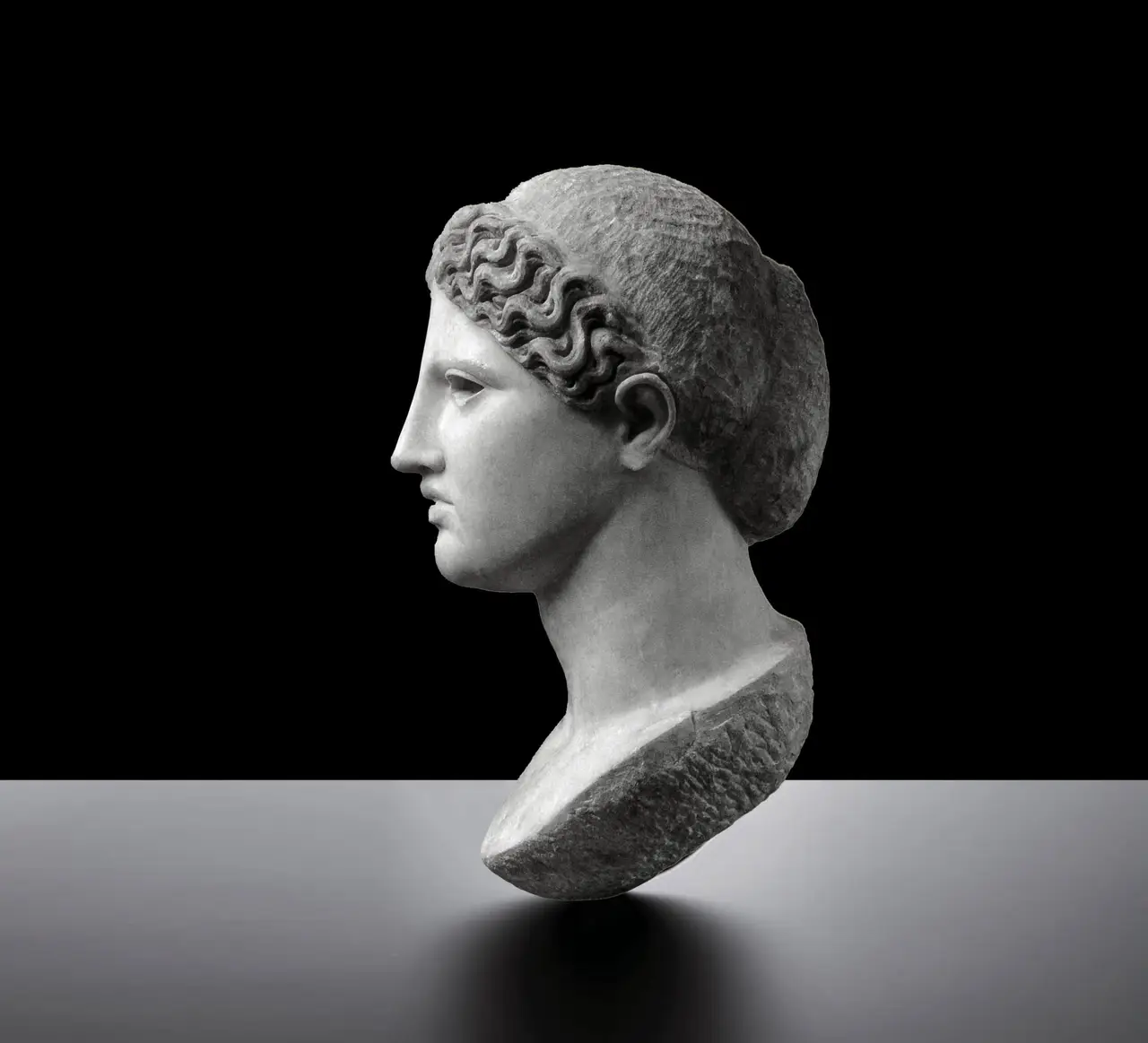 A Classical Greek marble head of a woman in profile, the hair waved back into a knot