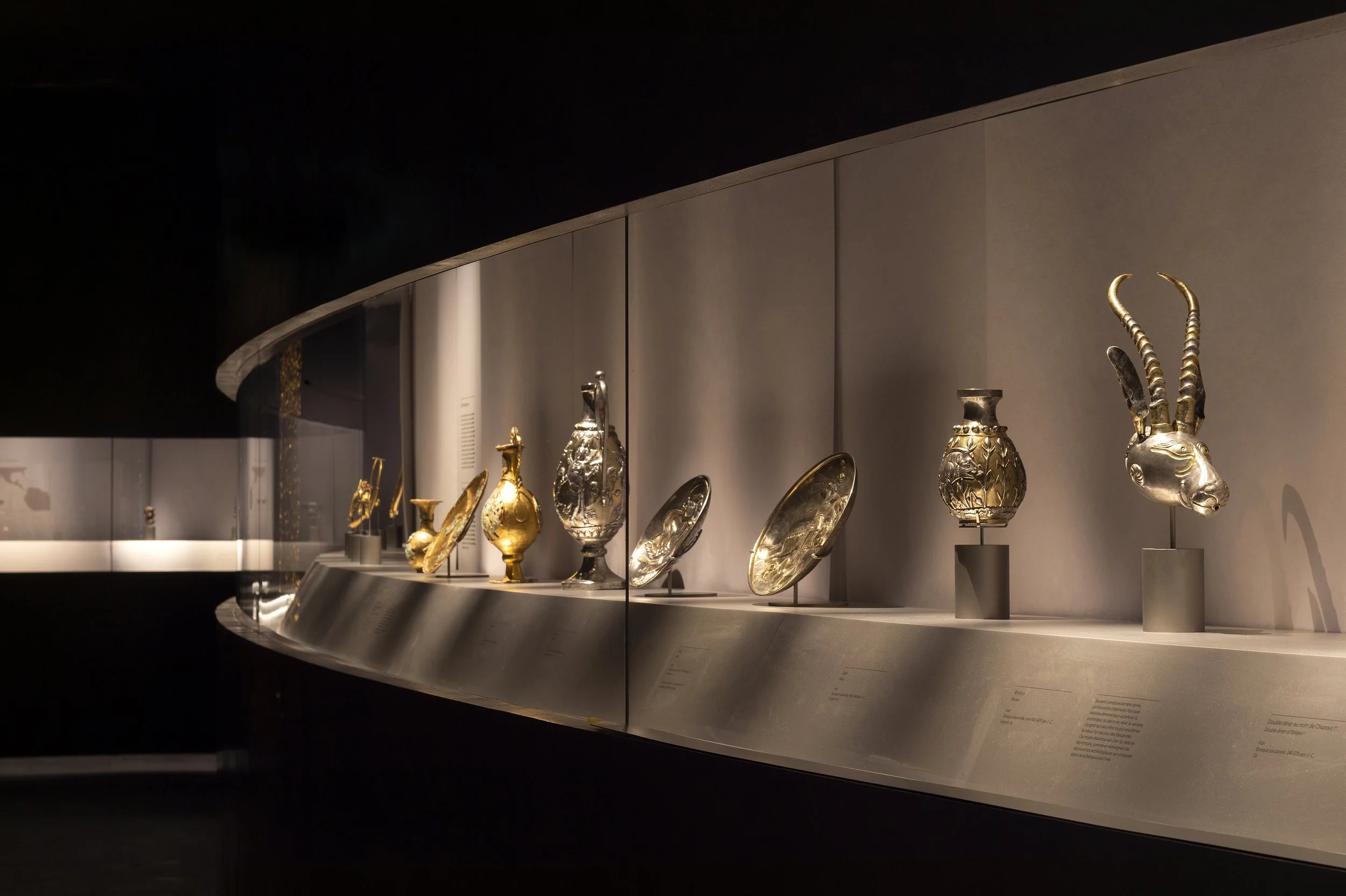 Gold and gilded vessels and a horned-animal rhyton in a long curving display case