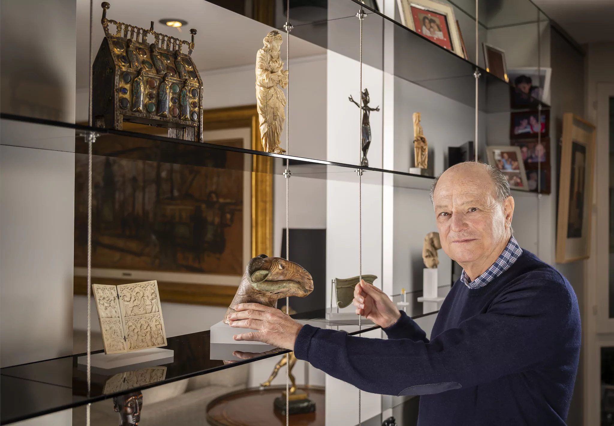 A collector handling an object before glass shelves holding a gilt reliquary, an ivory figure and a crucifix