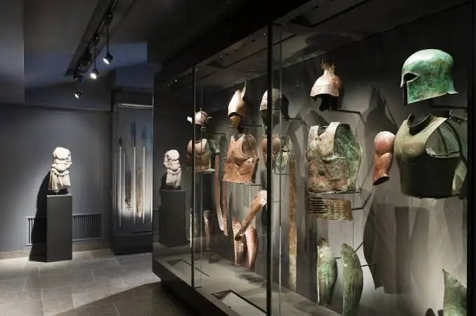 Ancient bronze helmets and cuirasses displayed in glass cases in a darkened gallery