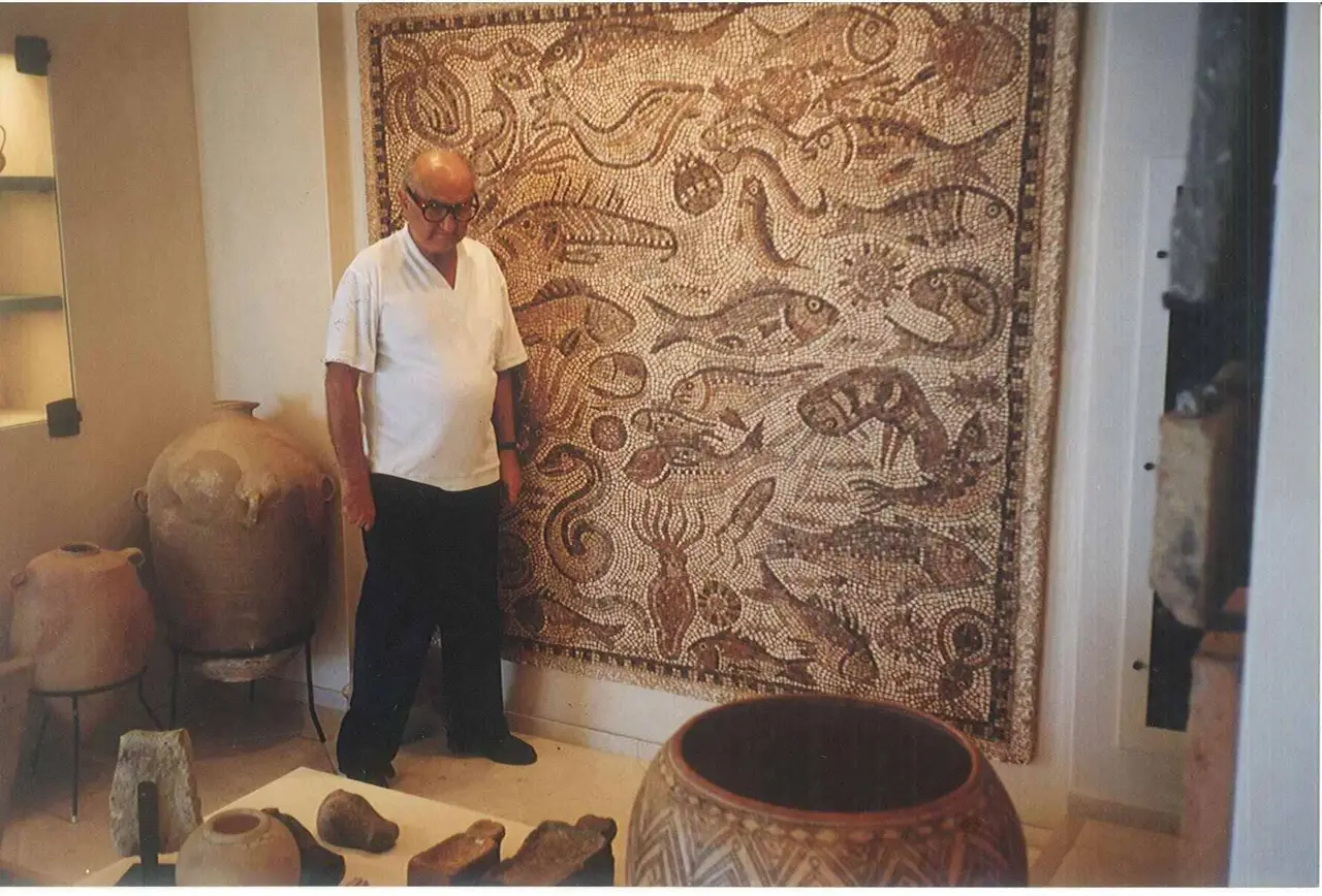 A collector standing before a large Roman marine mosaic, storage jars and antiquities around the room