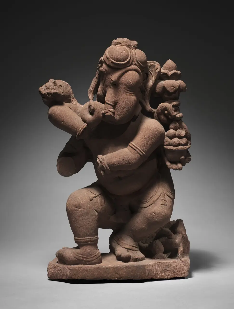 A crouching, potbellied dancing Gaṇeśa carved in sandstone