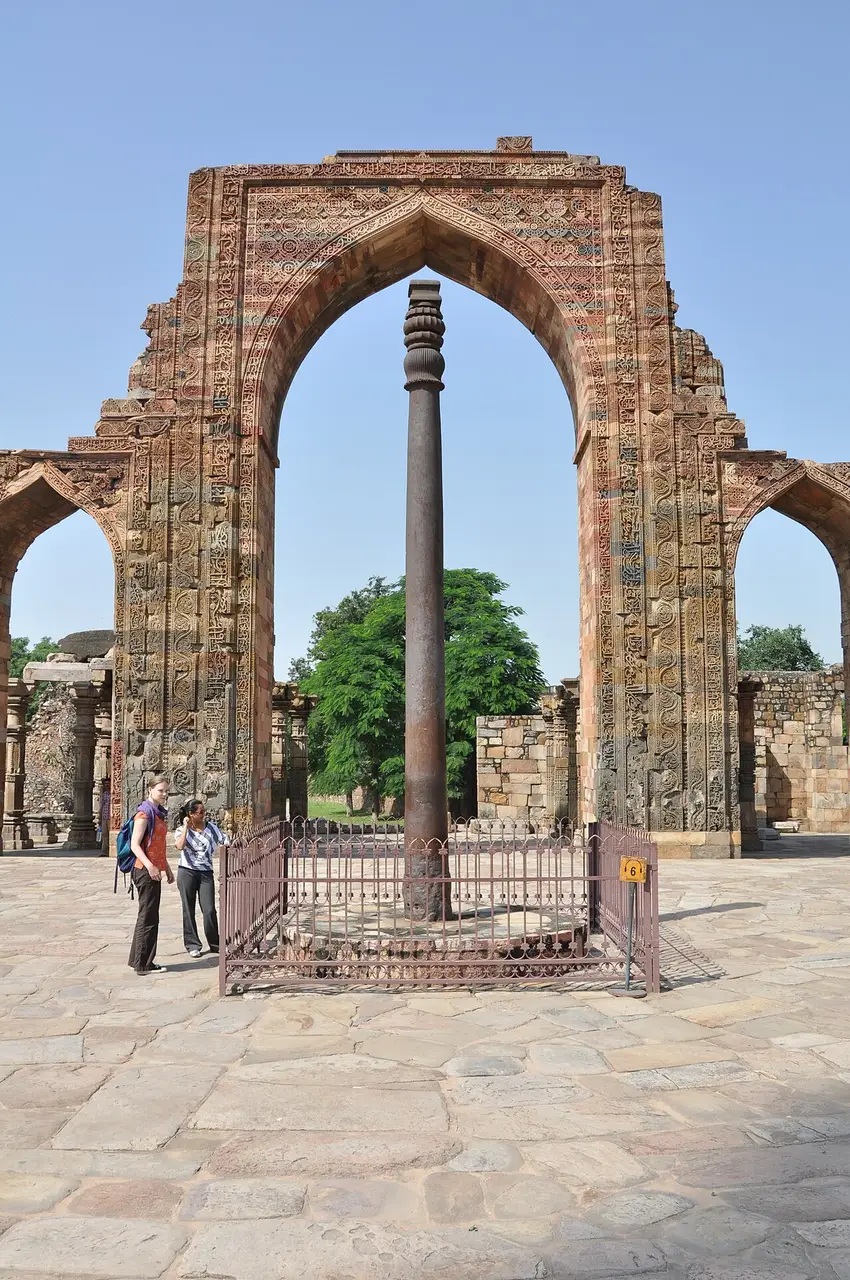 The Iron Pillar standing under a carved sandstone arch in the Qutb complex, Delhi